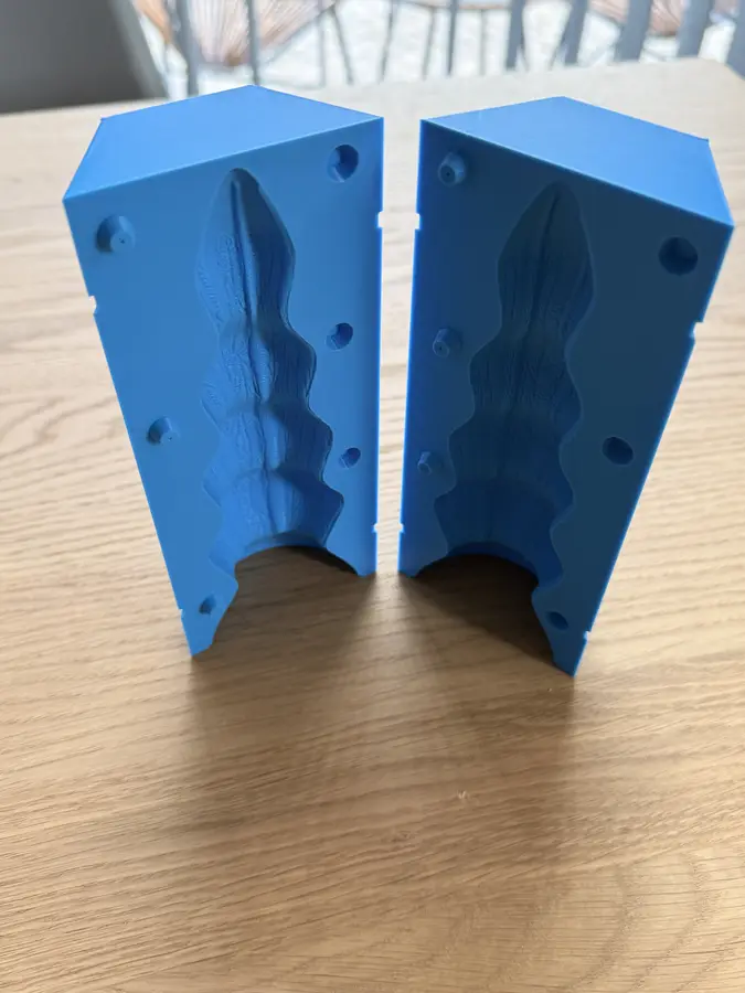Two blue printed mould halves standing on a table, each with the hollow of a ribbed toy down its middle.