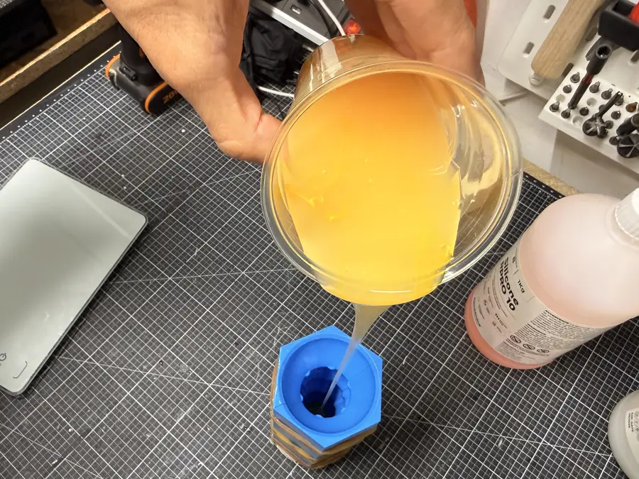 A thin stream of yellow silicone falls from a cup into the funnel of the second mould.