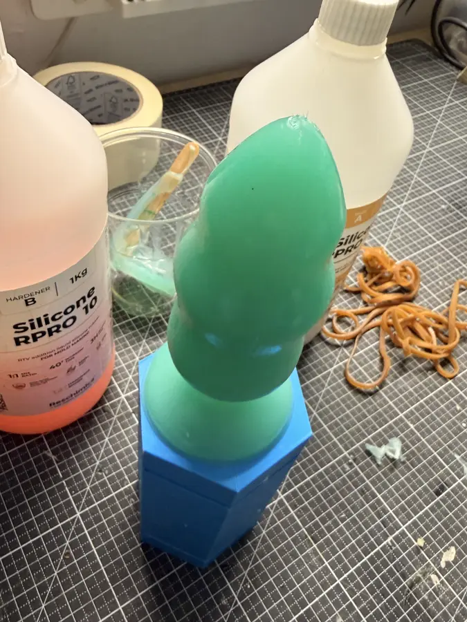 A green cast standing out of the bottom half of its mould, with the rubber bands beside it.